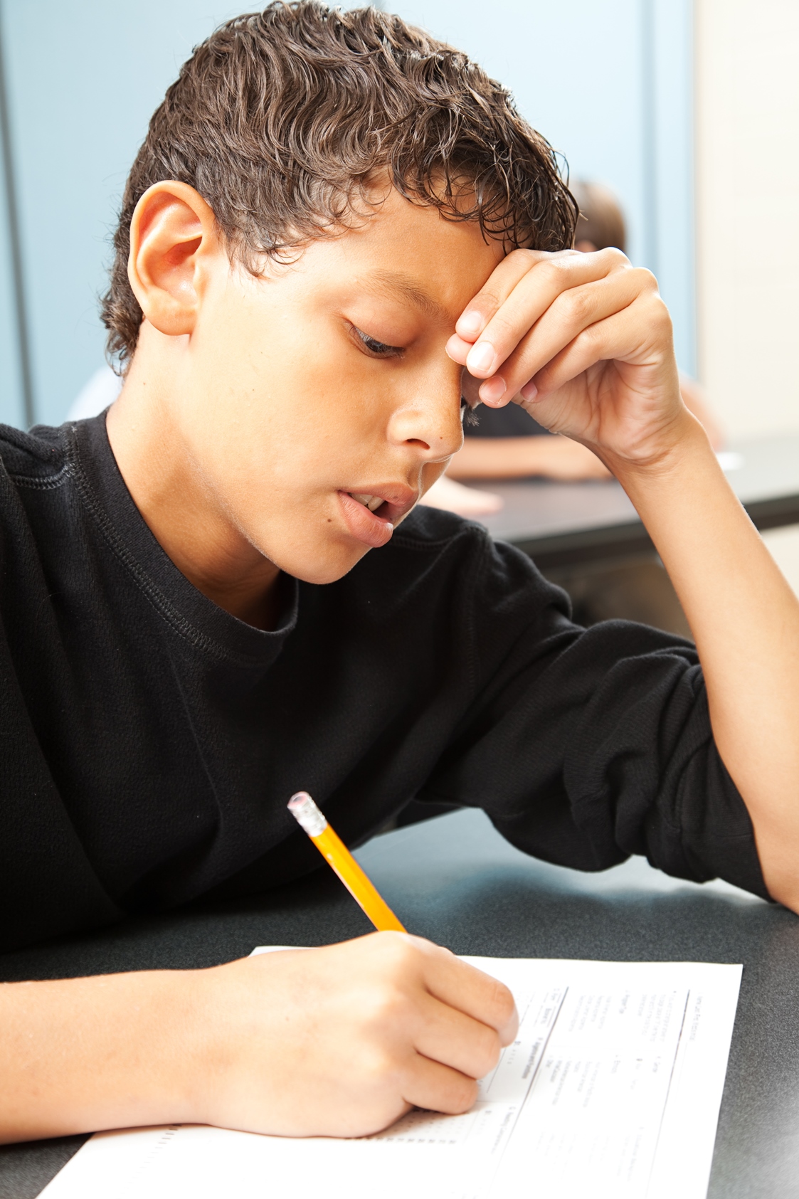 Stock photo showing school aged boy writing on school work and holding head with one hand